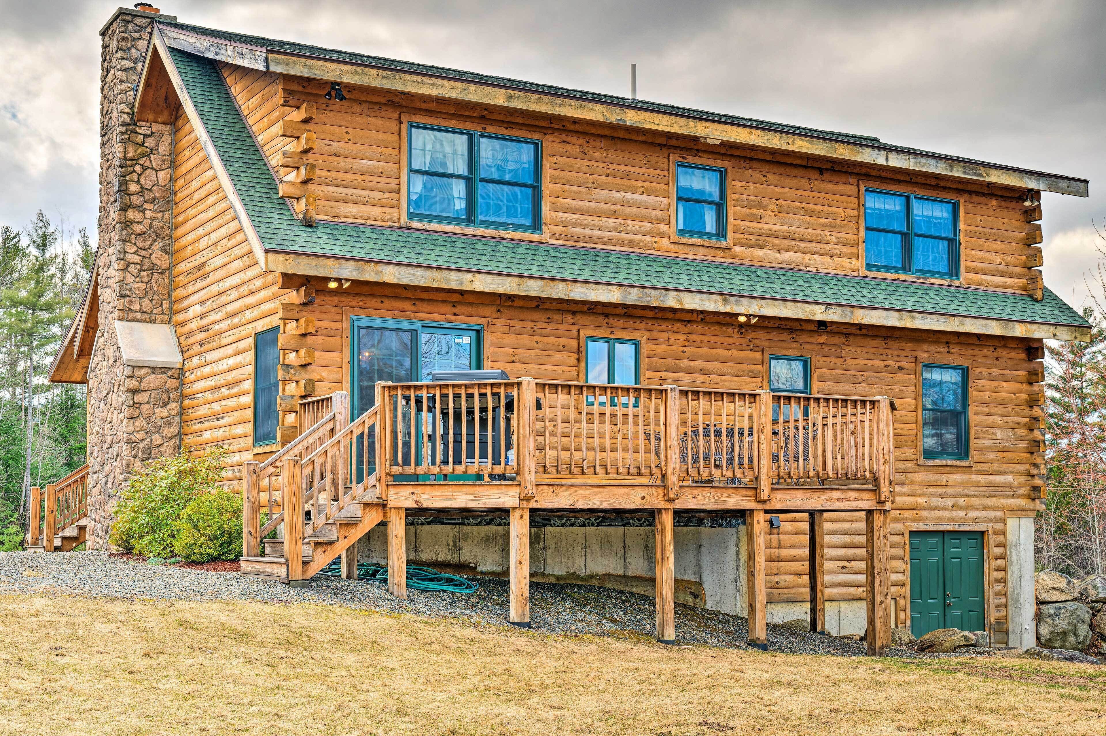 A log cabin with a stone chimney, a balcony, and a green roof.