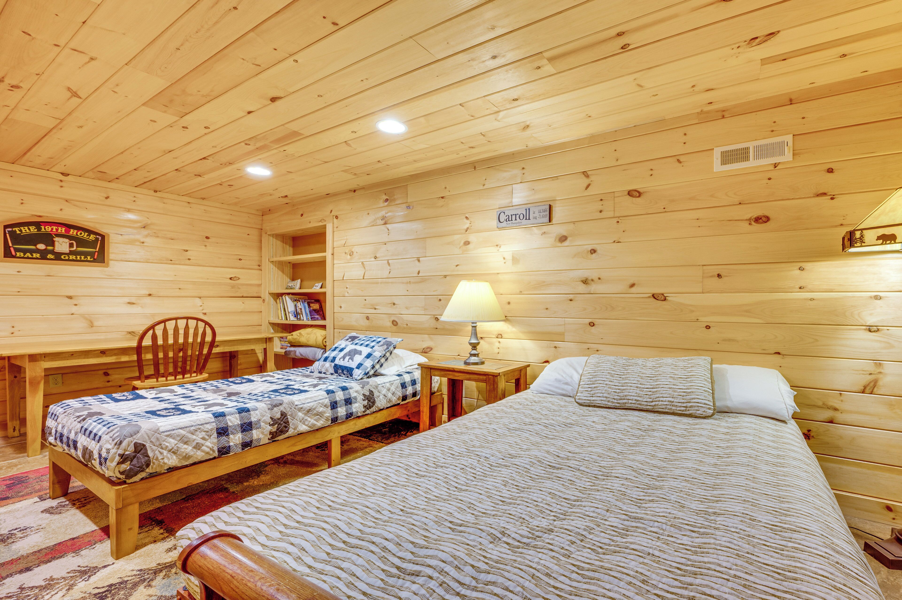 A wooden cabin room with two beds, a desk, a chair, and a bookshelf.