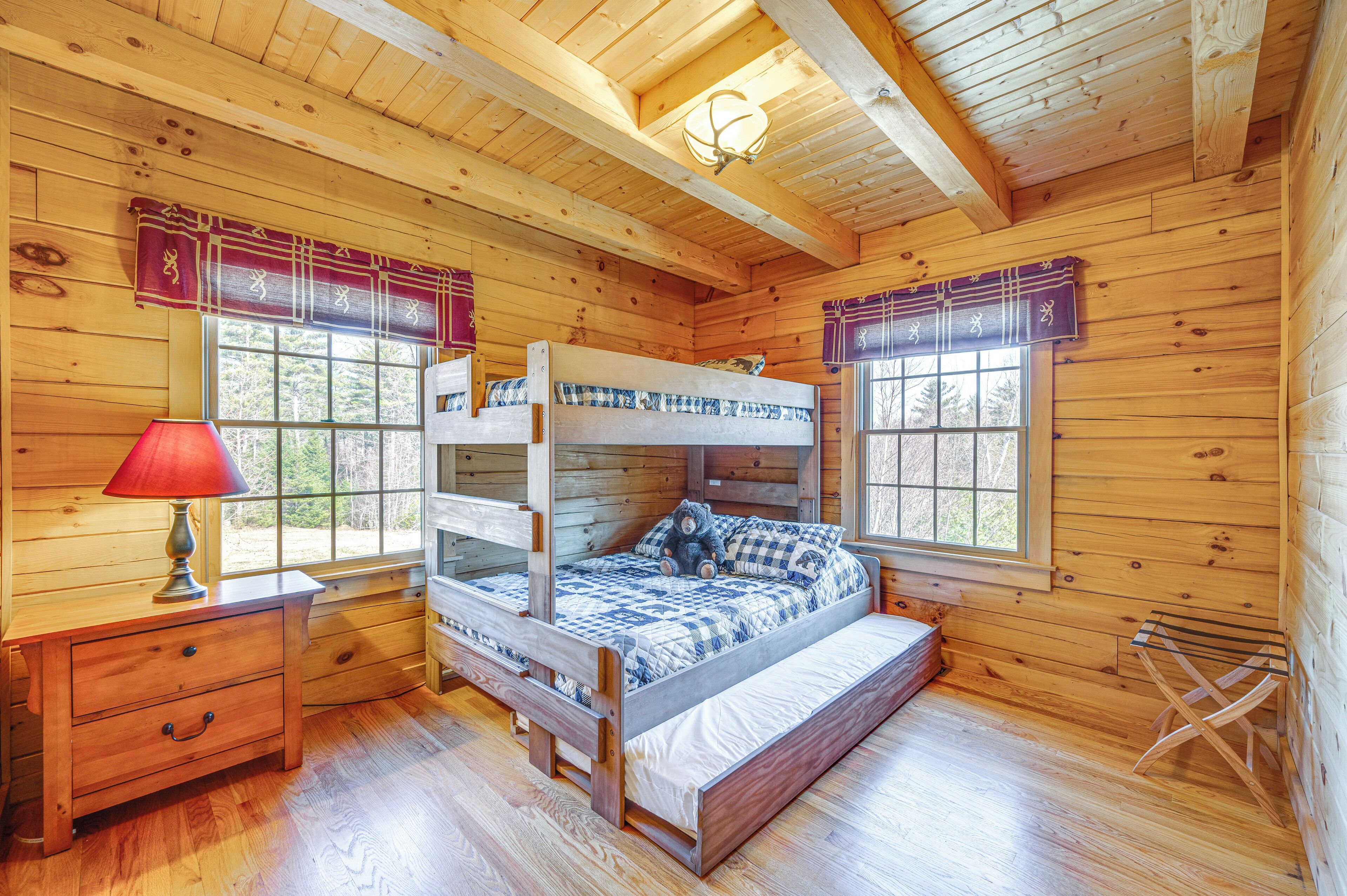 A wooden cabin bedroom with bunk beds, a nightstand, a lamp, and a window with curtains.