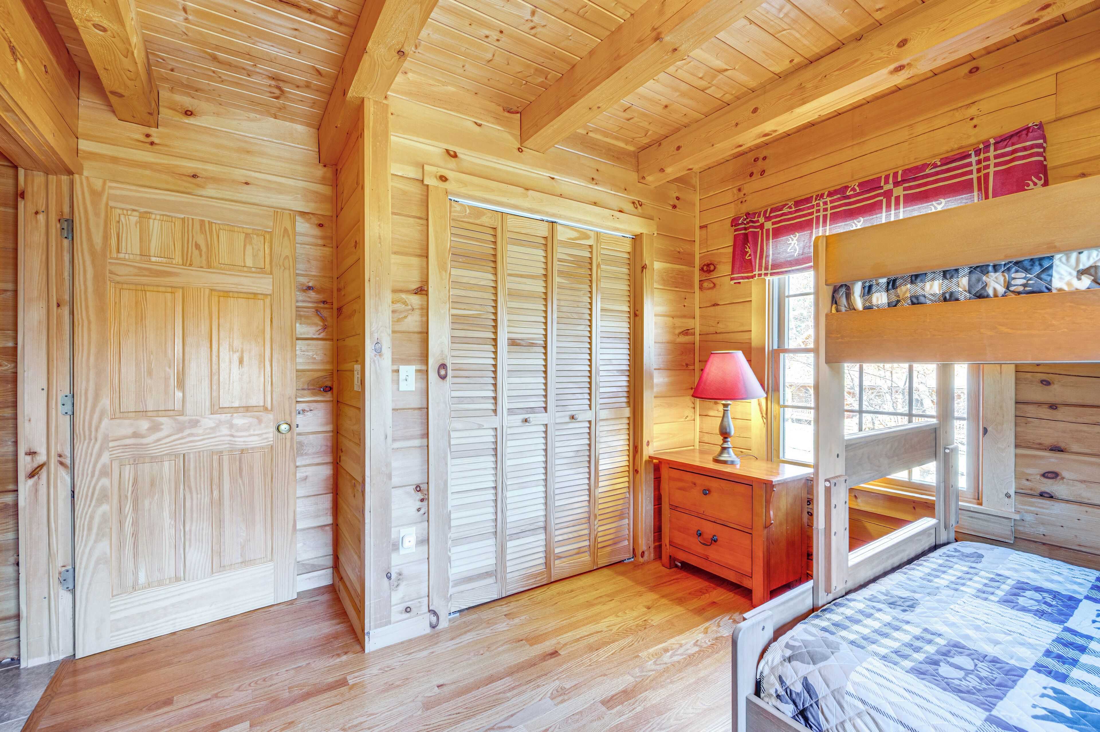 A wooden cabin bedroom with a bunk bed, wooden wardrobe, and a nightstand with a lamp.