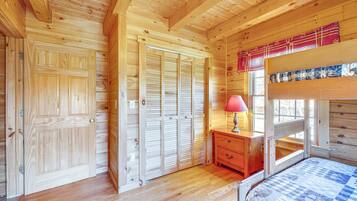 A wooden cabin bedroom with a bunk bed, wooden wardrobe, and a nightstand with a lamp.
