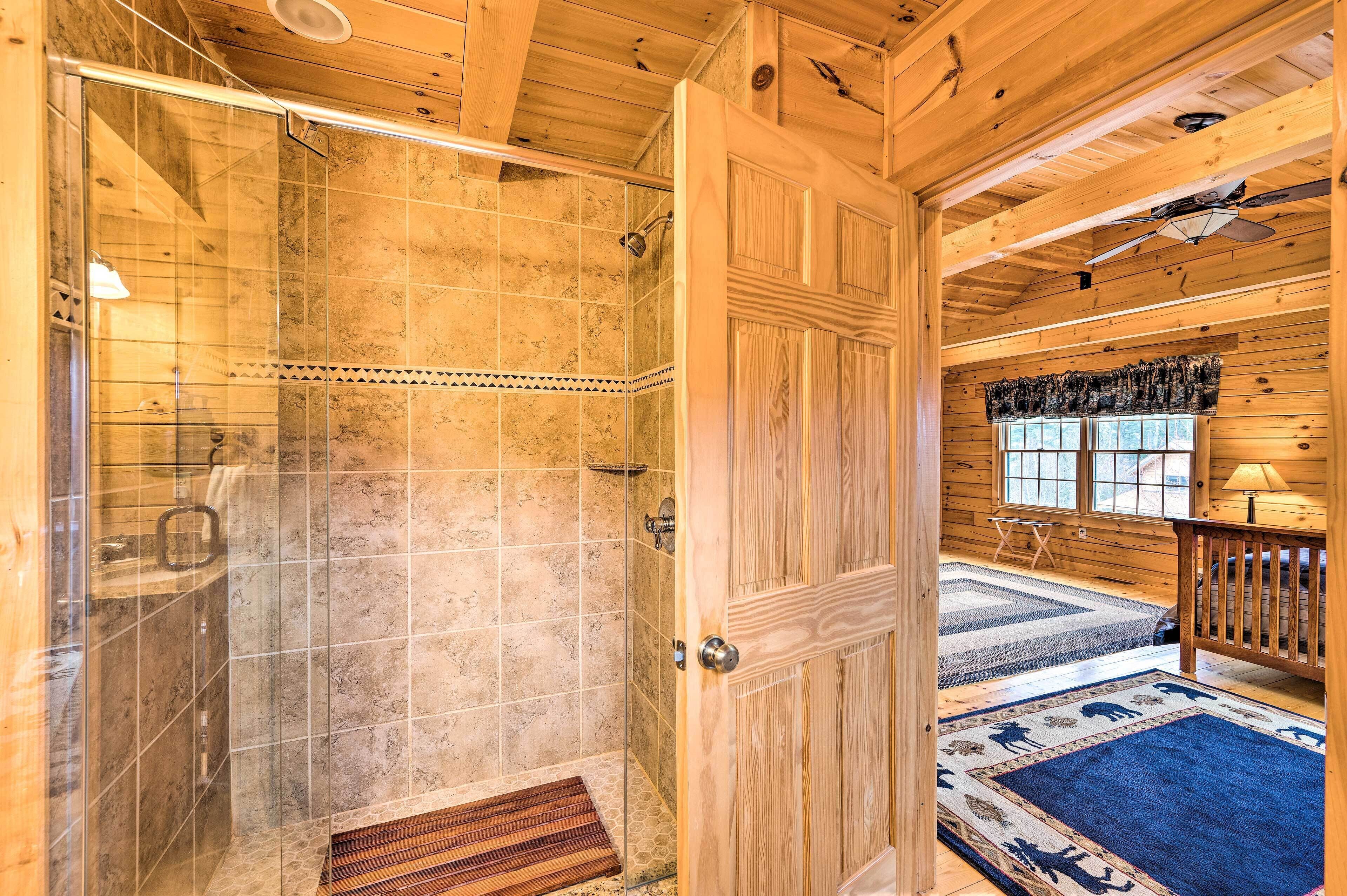 A wooden cabin interior with a glass shower, a wooden door, a window with curtains, and a blue rug.