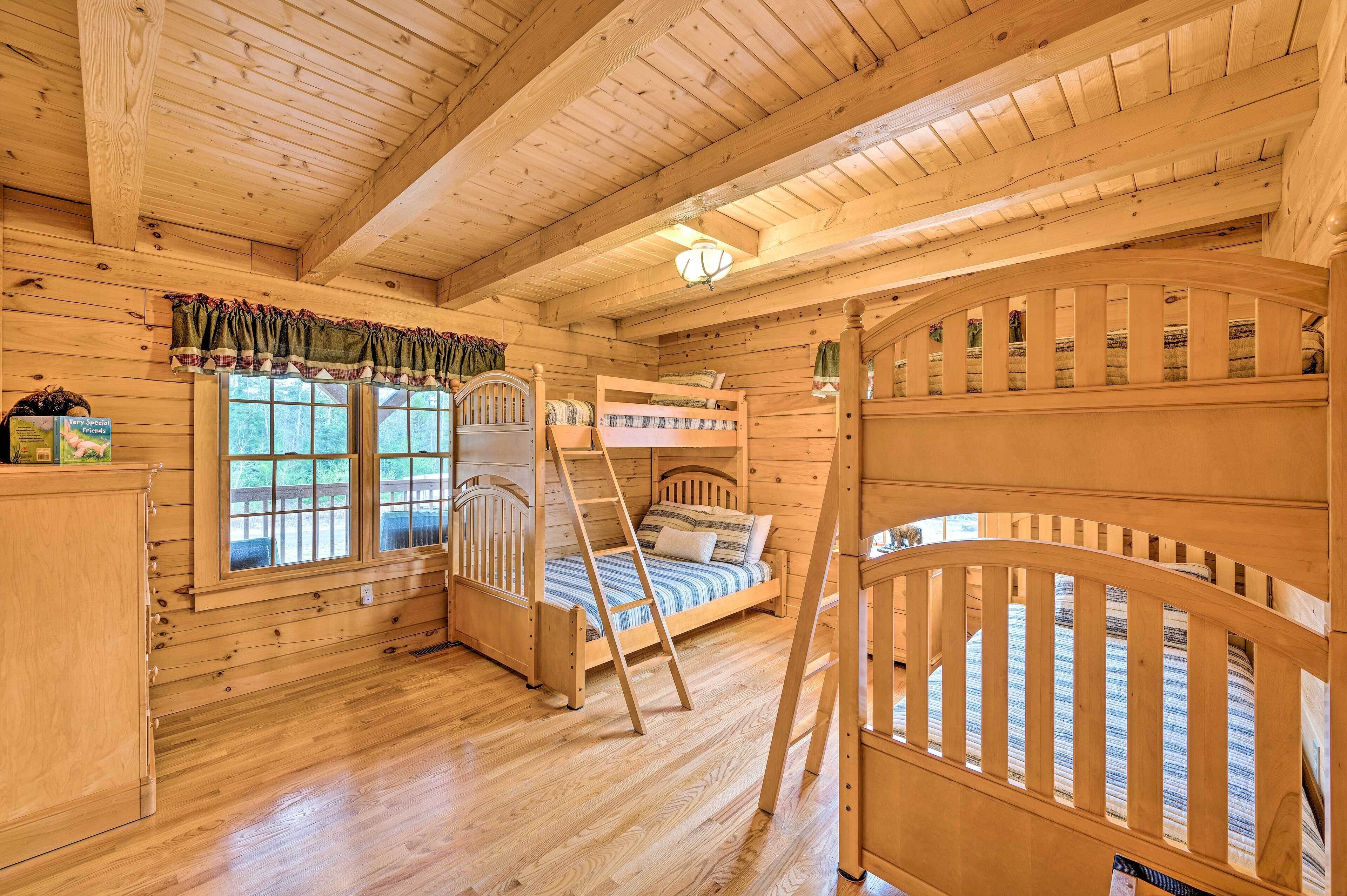 A wooden cabin room with bunk beds, a ladder, and a window with a view of the outdoors.
