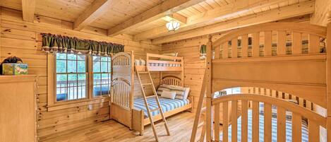 A wooden cabin room with bunk beds, a ladder, and a window with a view of the outdoors.