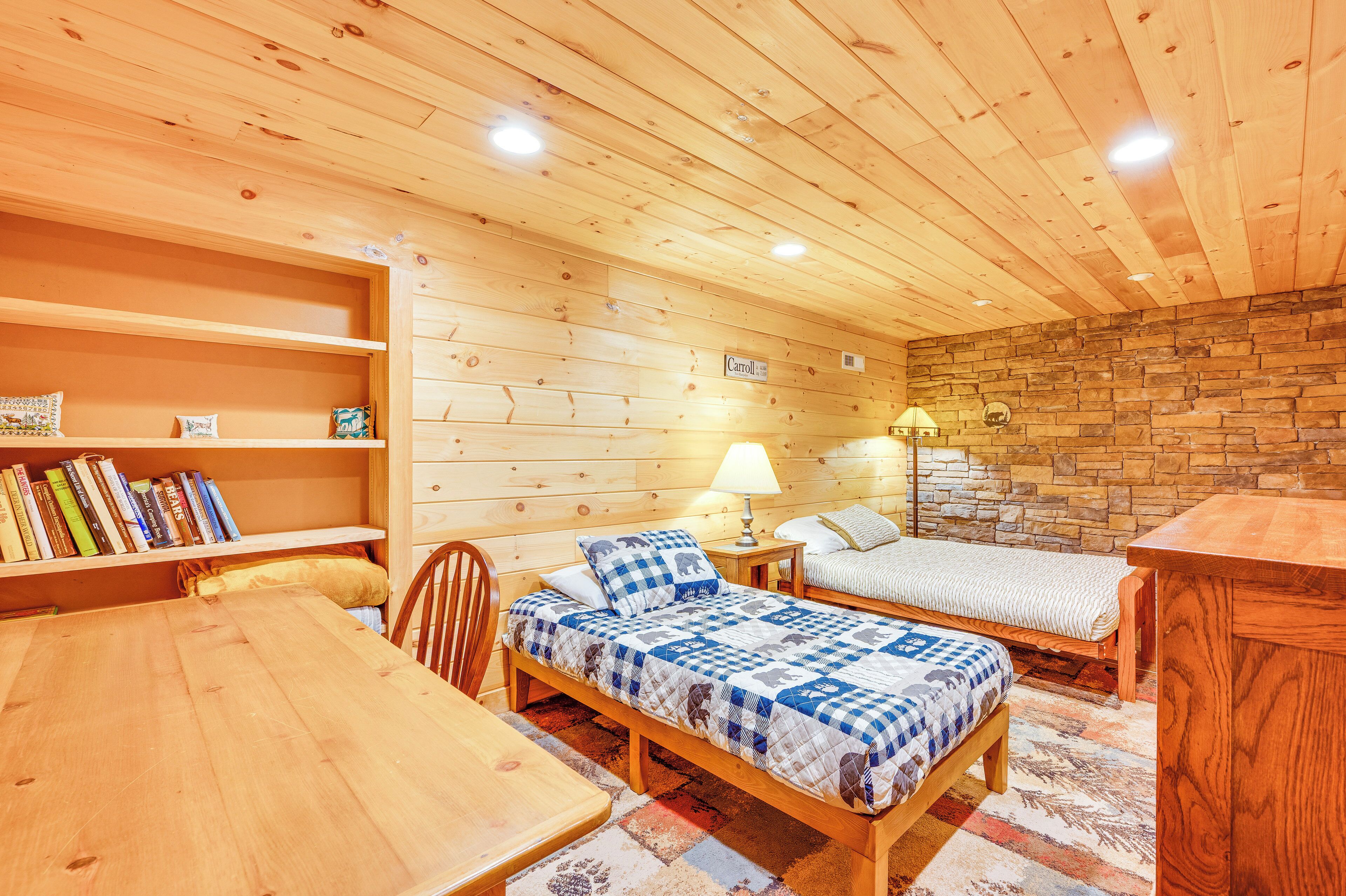 Acogedora habitación tipo cabaña de madera con dos camas, una mesa de comedor y una estantería llena de libros.
