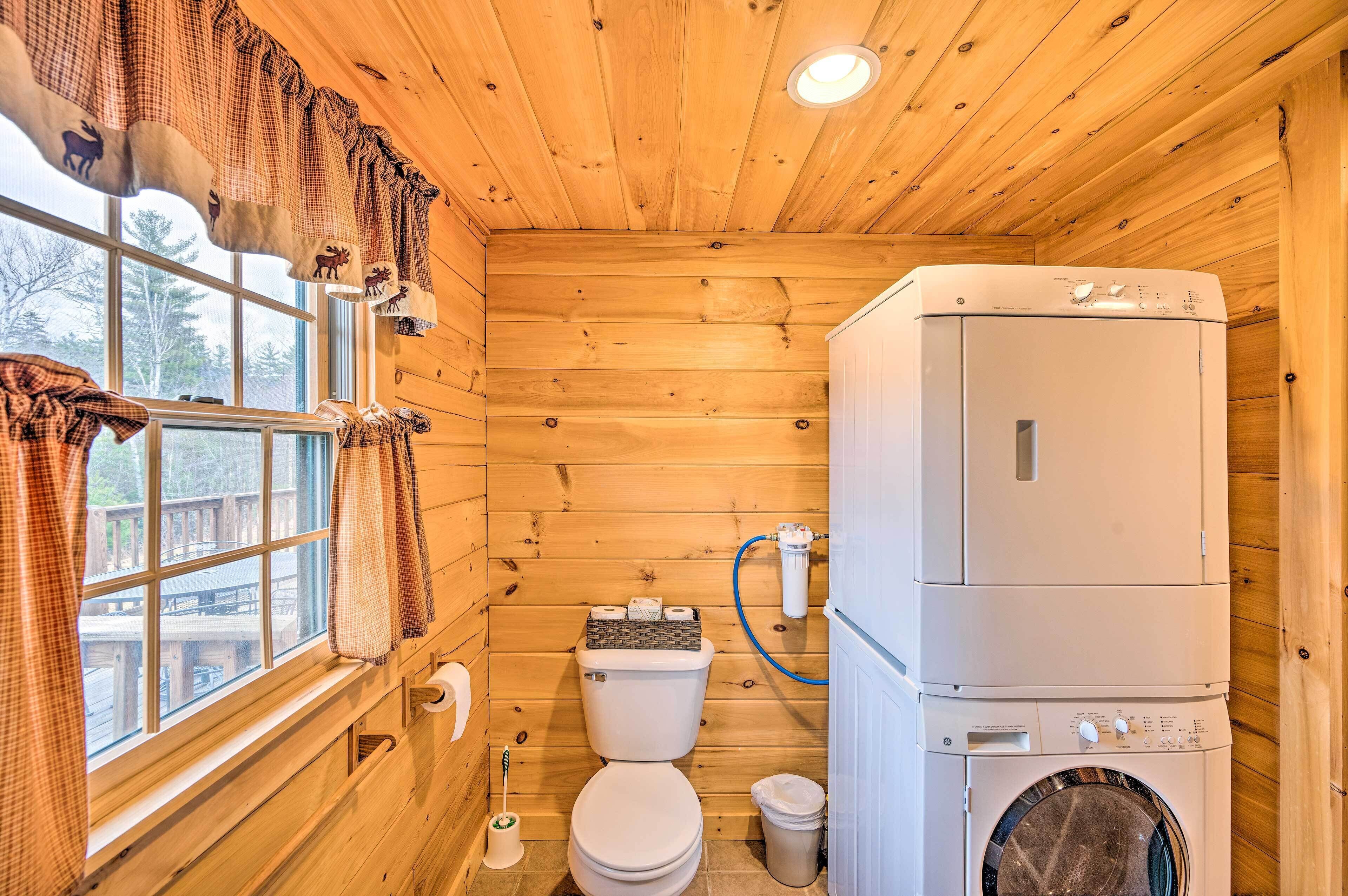 A compact wooden bathroom with a toilet, washing machine, and a window.