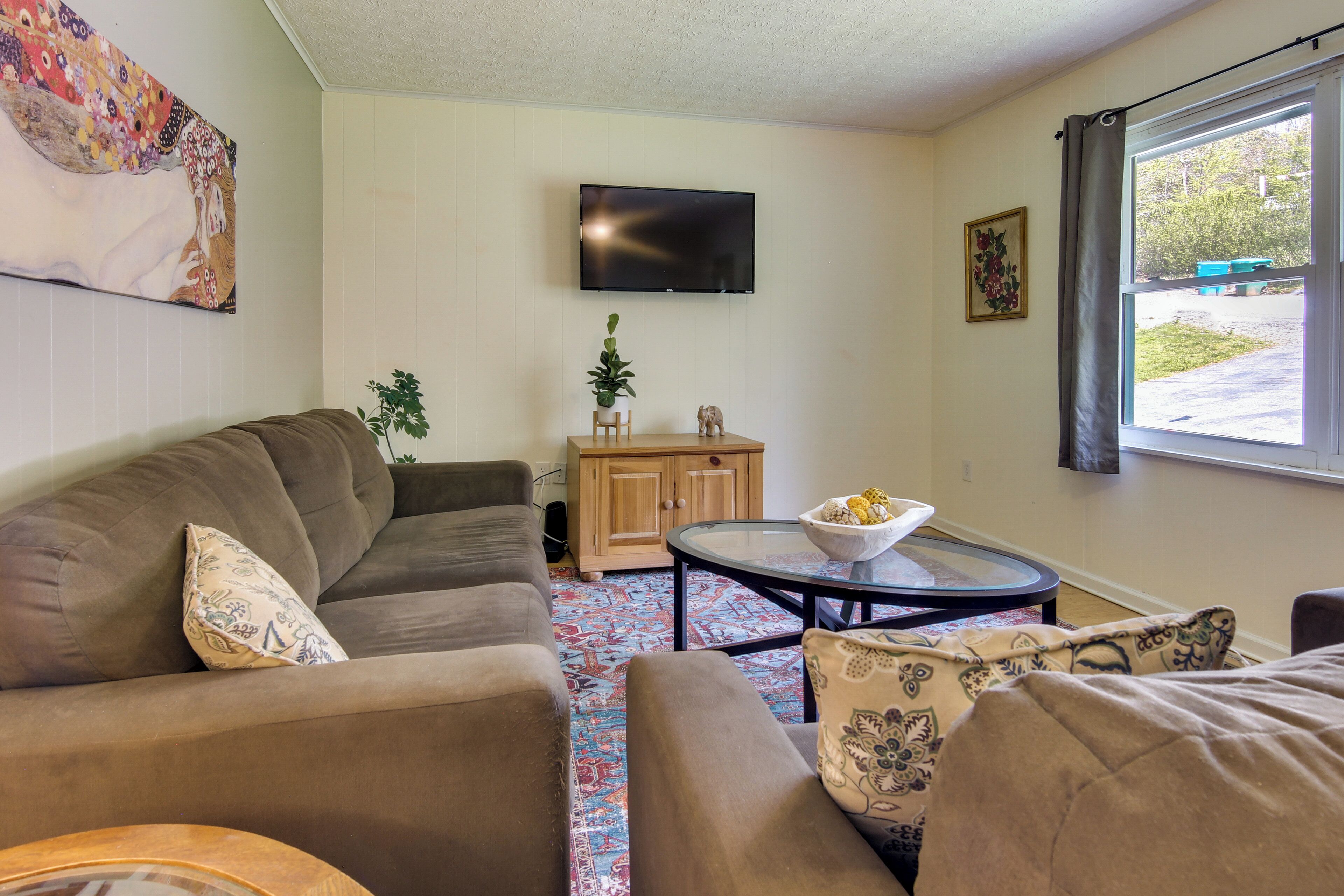 A living room with a sofa, a coffee table, a flat-screen TV, a cabinet, and a window with a view of the outdoors.