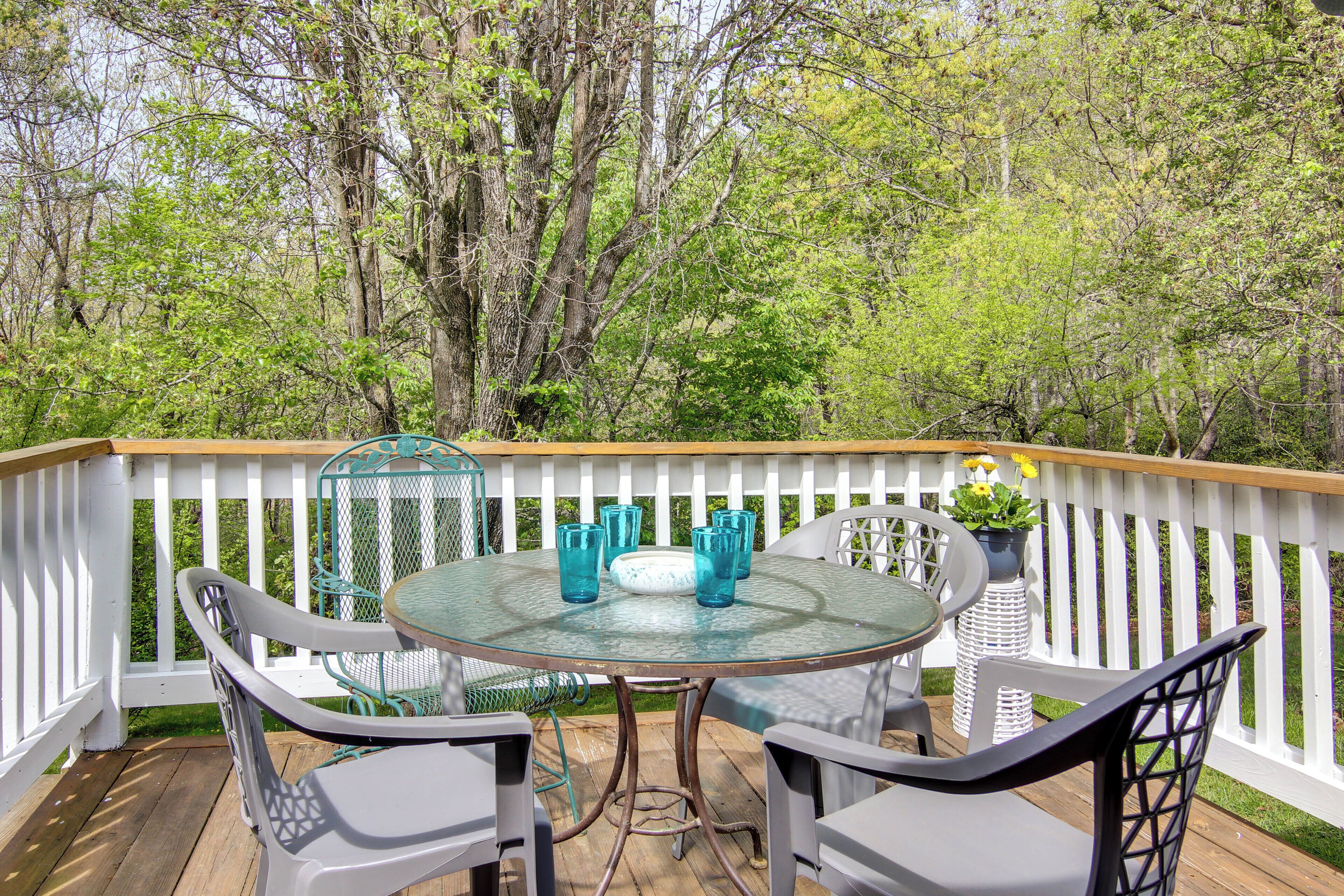 A round glass table with four chairs on a wooden deck, surrounded by a white picket fence.