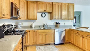 A kitchen with wooden cabinets, a stainless steel dishwasher, a stove, and a clock on the wall. - Pet-friendly Black Mountain Vacation Home w/ Deck (Black Mountain)