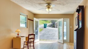 A room with a wooden floor, a ceiling fan, a desk with a lamp, a chair, and a door leading outside. - Pet-friendly Black Mountain Vacation Home w/ Deck (Black Mountain)