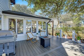 A covered outdoor deck with a grill, two lounge chairs, and a small table with a fire pit. - Waterfront Pine Knoll Shores Gem w/ Boat Dock (Atlantic Beach)