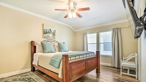 A bedroom with a wooden bed, a ceiling fan, a window with curtains, and a white chair. - Pet-friendly Home w/ Pool, 25 Mi to Austin! (Leander)
