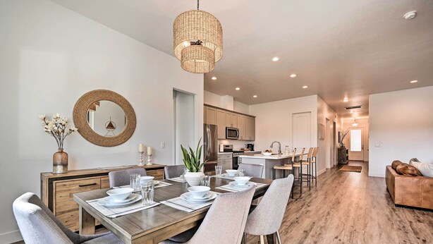 A modern dining area with a wooden table set for six, surrounded by grey upholstered chairs. A woven pendant light hangs above, and a round mirror is mounted on the wall. - Flagstaff Retreat w/ Covered Patio, 3 Mi to Dtwn (Flagstaff)