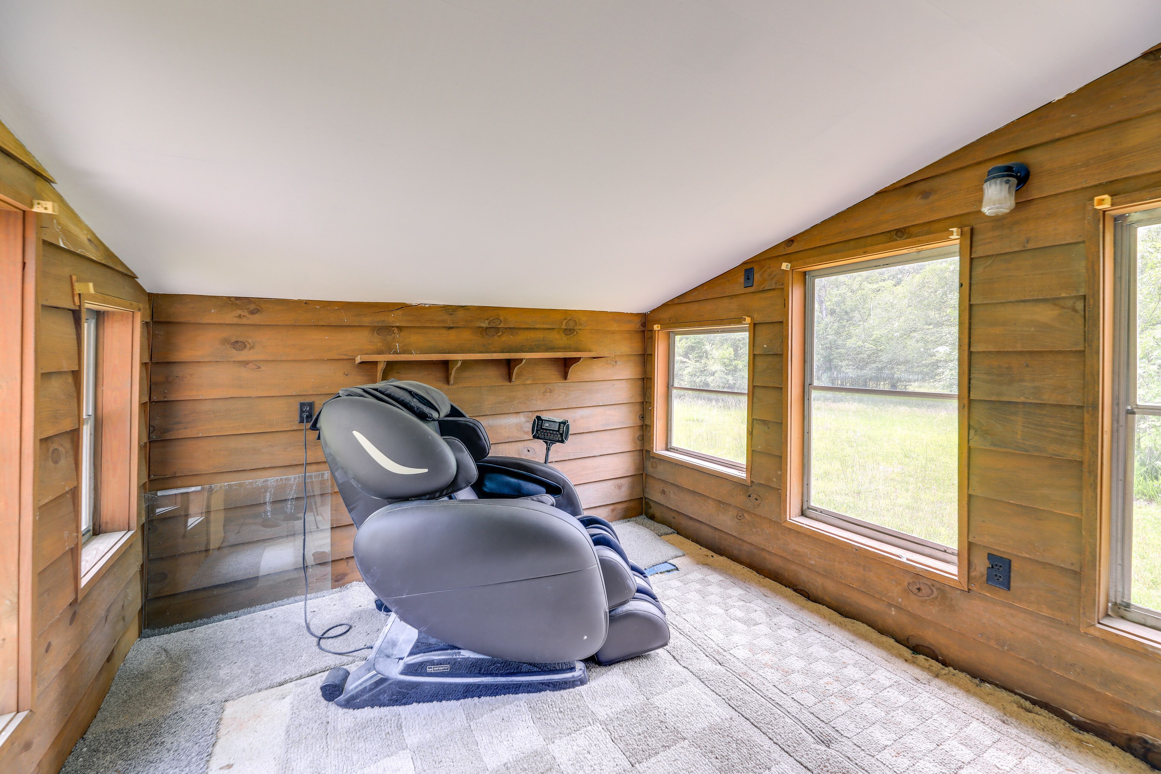 Ein Massagesessel in einem Holzraum mit großen Fenstern und einer Deckenleuchte.