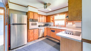 A compact kitchen with wooden cabinets, a stainless steel refrigerator, a microwave, a toaster, a dishwasher, and a gas stove. - North Carolina Getaway Near Kayaking & Fishing! (Oriental)
