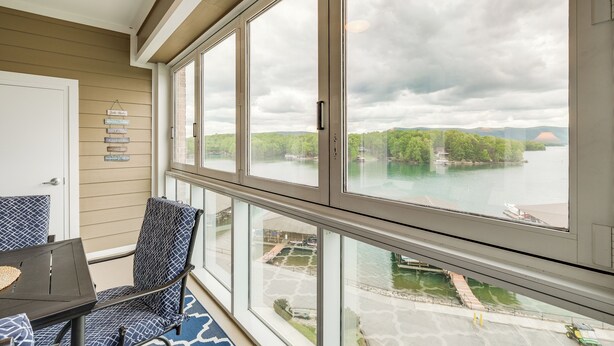 A balcony with large windows overlooking a body of water, a chair, and a table.