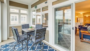 A sunlit patio with a dining table and chairs, large windows, and a sliding glass door leading to a living area.