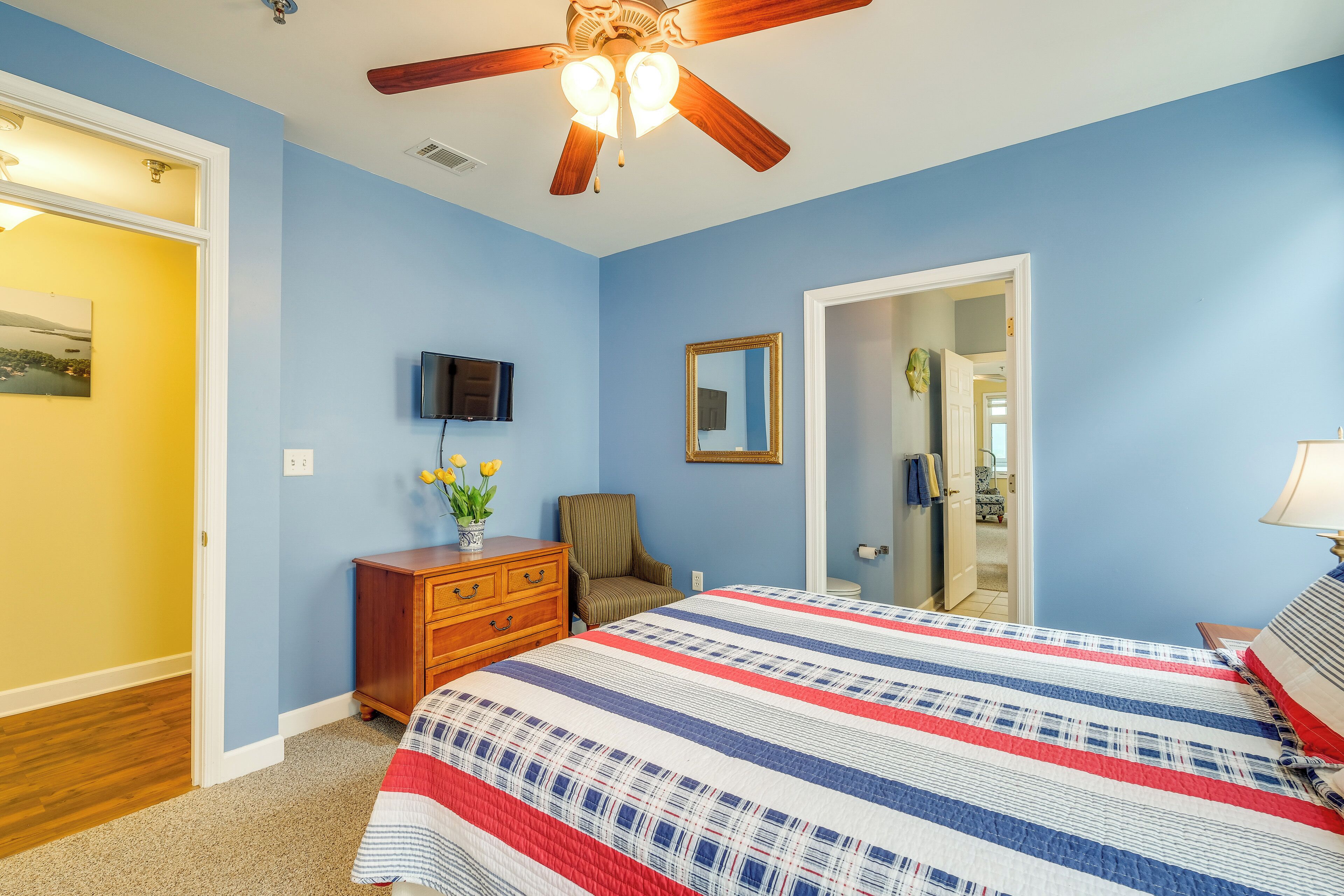 A bedroom with a bed, a ceiling fan, a dresser, a chair, a TV, and a mirror.