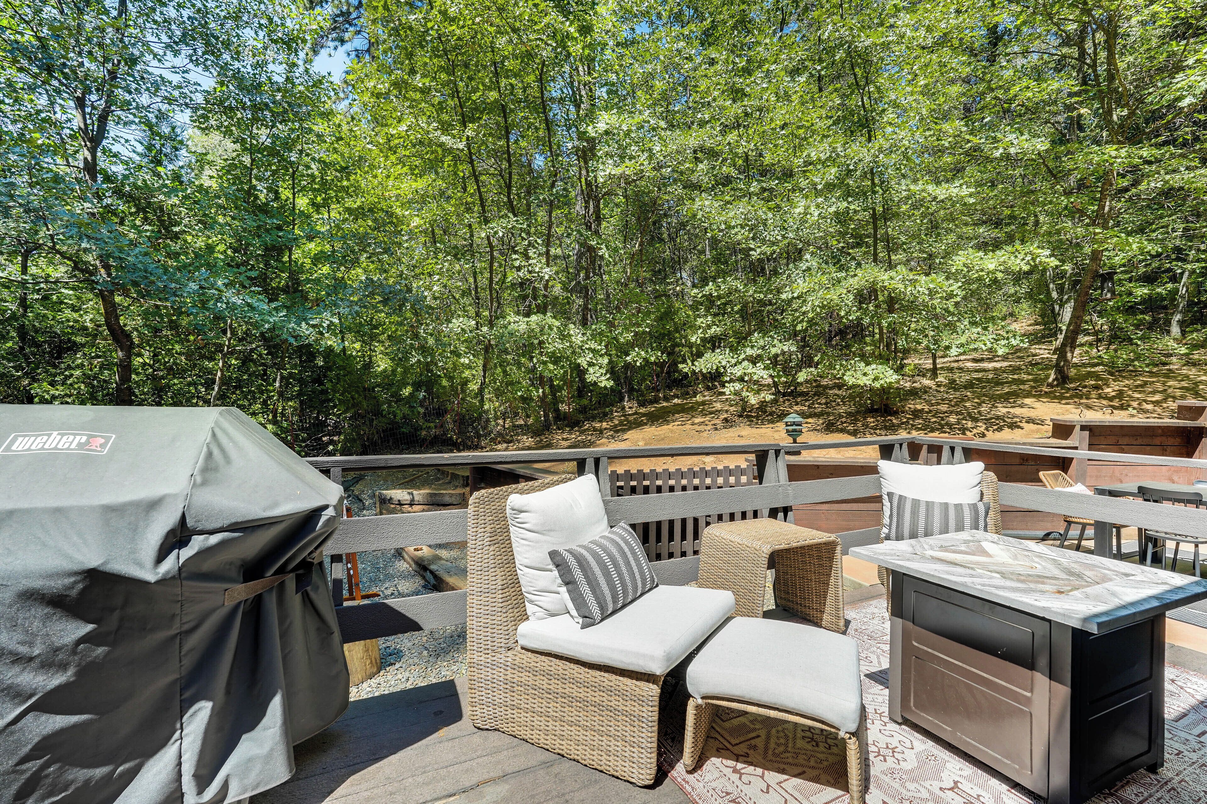 Une terrasse extérieure aménagée avec des meubles en osier, un barbecue et une vue sur une zone boisée.