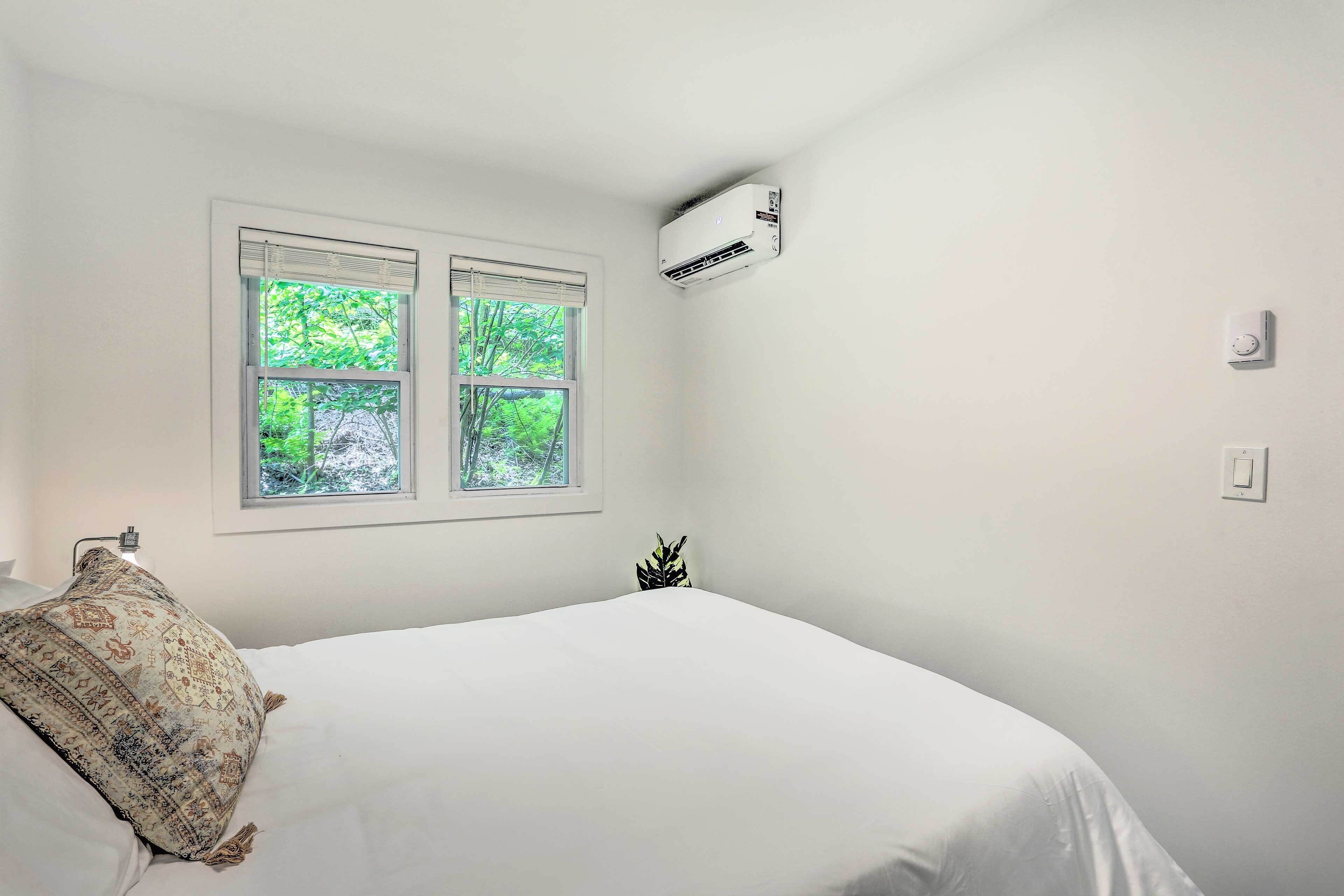 A bedroom with a bed, two windows, an air conditioning unit, and a wall-mounted light switch.