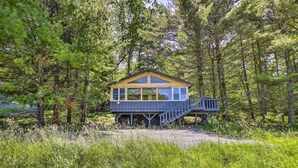 A wooden cabin with a deck and stairs, surrounded by dense forest. - Catskills Sanctuary w/ Lake Access + Hot Tub (Narrowsburg)