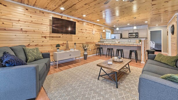 A cozy living room with a wooden ceiling, a flat-screen TV, a dining table, and a kitchen area with bar stools. - Cozy Elmira Cabin ~ 23 Mi to Boyne Mountain Resort (Mancelona)