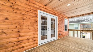 A wooden deck with a glass door leading to a covered porch area. - Cozy Elmira Cabin ~ 23 Mi to Boyne Mountain Resort (Mancelona)