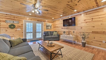 A cozy living room with a wooden ceiling, a gray sofa, a wooden coffee table, and a flat-screen TV mounted on the wall.
