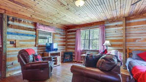 A log cabin interior with a fireplace, leather sofas, and a television. - Historic Log Cabin w/ Porch Near Patoka Lake! (Taswell)