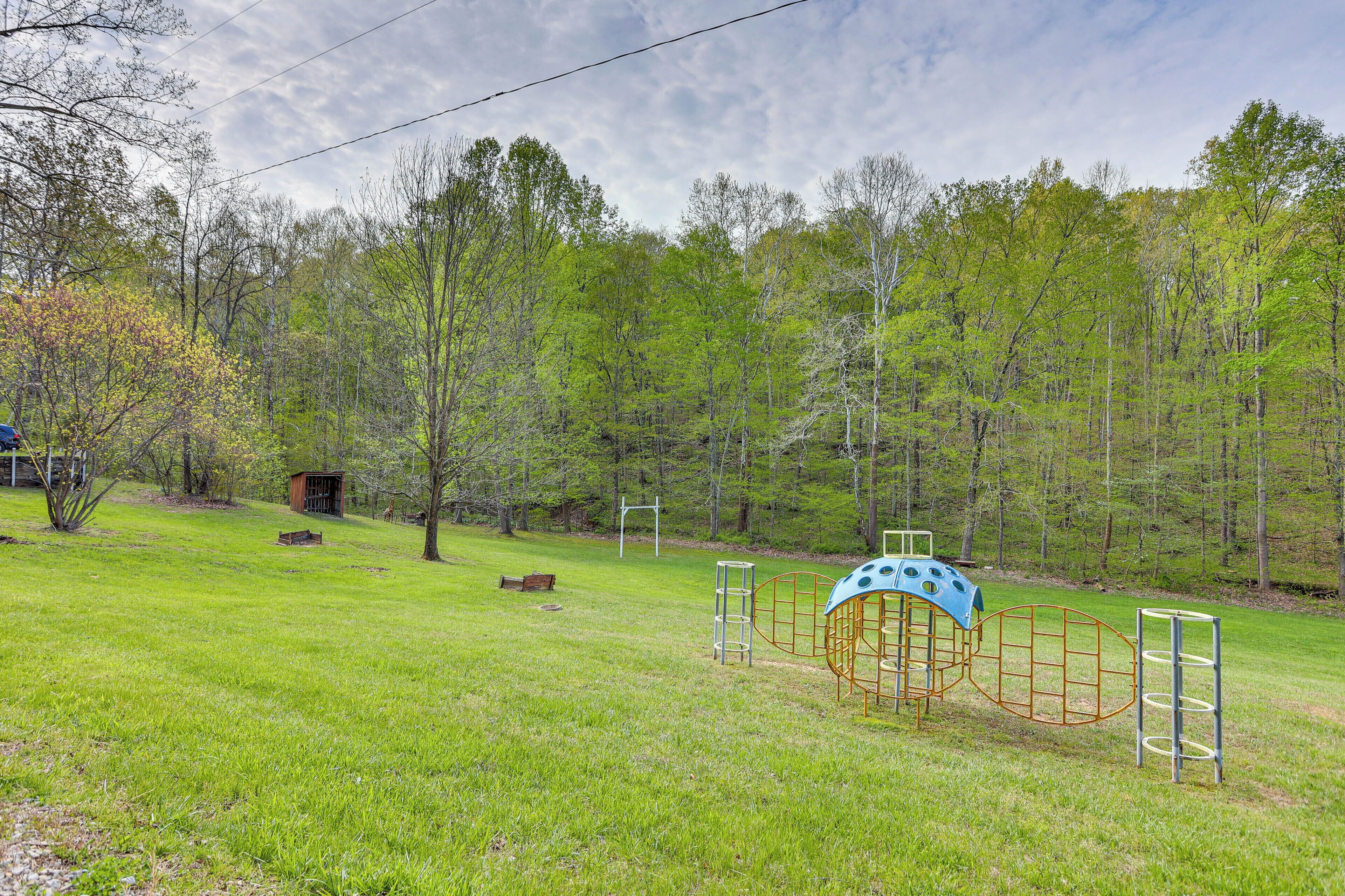 A playground with climbing structures and a small shed in a grassy field with trees in the background.