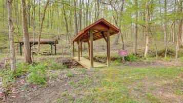 A wooden gazebo in a forested area with a picnic table nearby.