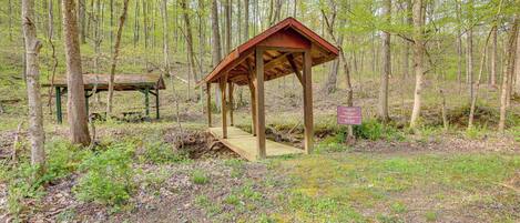 A wooden gazebo in a forested area with a picnic table nearby.