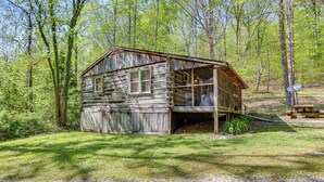 A rustic cabin with a porch, surrounded by a forest. - Historic Log Cabin w/ Porch Near Patoka Lake! (Taswell)