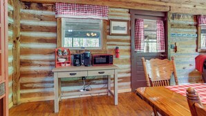 A wooden cabin interior with a wooden desk, a microwave, a coffee maker, and a chair. - Historic Log Cabin w/ Porch Near Patoka Lake! (Taswell)