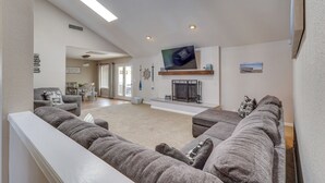 A living room with a large sectional sofa, a flat-screen TV mounted on the wall, a fireplace, and a dining area in the background. - 3,000 Sq Ft & Large Yard! 5BR Lake Havasu Home (Lake Havasu City)