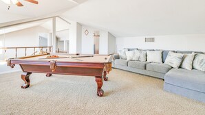 A spacious living room with a pool table, a grey sofa, and a staircase leading to an upper level. - 3,000 Sq Ft & Large Yard! 5BR Lake Havasu Home (Lake Havasu City)