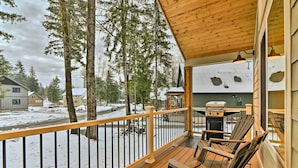 A wooden deck with a railing, outdoor seating, and a view of a snowy landscape with trees and houses. - Family-friendly Packwood Retreat w/ Deck! (Packwood)