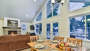 A dining area with a wooden table set for four, a stone fireplace, and a view of a snowy landscape through large windows. - Family-friendly Packwood Retreat w/ Deck! (Packwood)