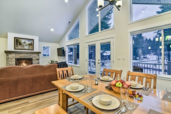 A dining area with a wooden table set for four, a stone fireplace, and a view of a snowy landscape through large windows. - Family-friendly Packwood Retreat w/ Deck! (Packwood)