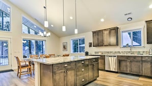 A spacious kitchen with a large island, dark wooden cabinets, and a view of the outdoors through large windows. - Family-friendly Packwood Retreat w/ Deck! (Packwood)
