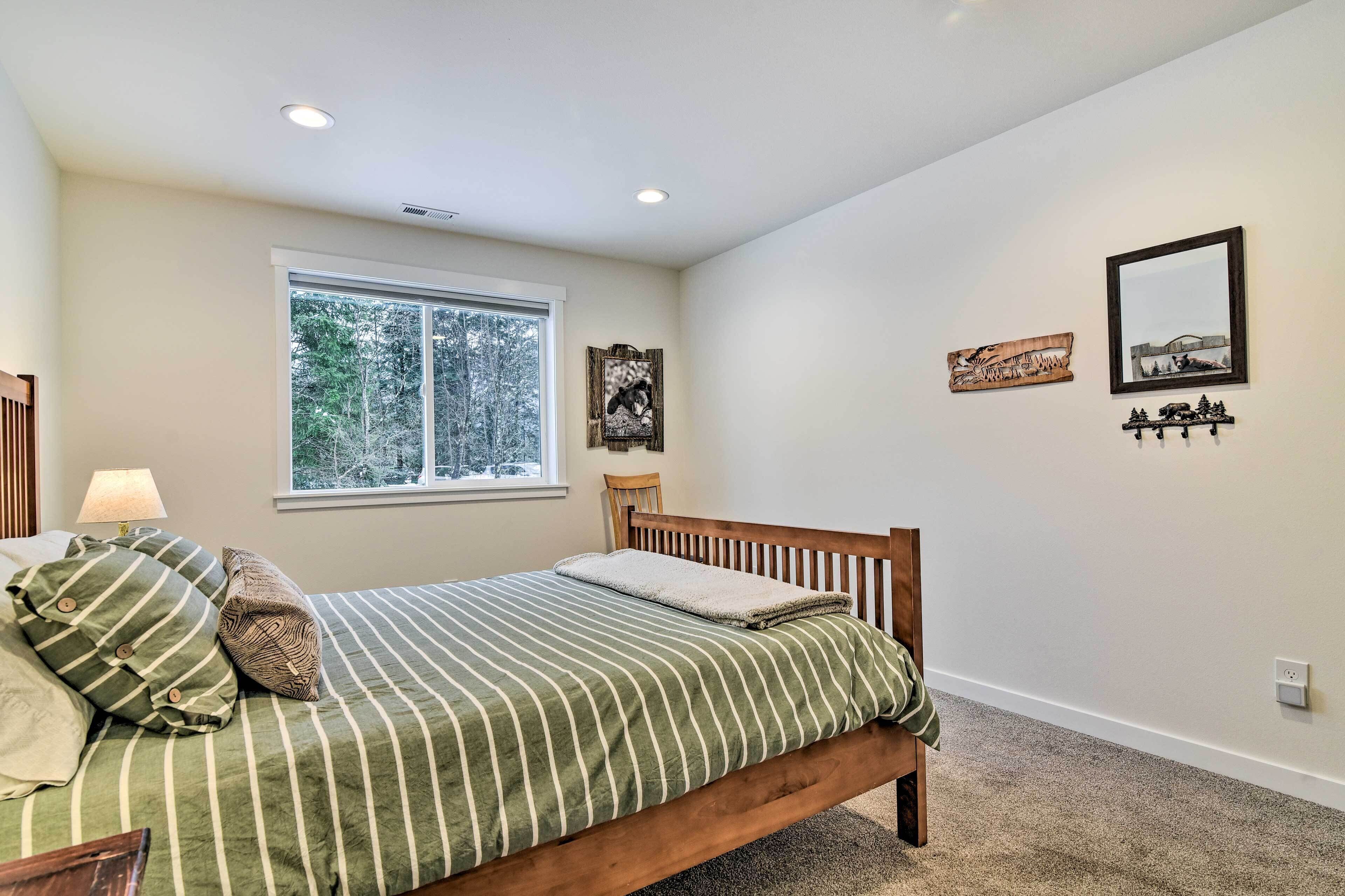 A bedroom with a large window, a bed with striped bedding, a wooden headboard, and wall-mounted decorations.