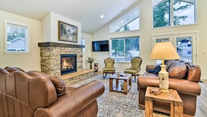 A spacious living room with a stone fireplace, leather sofas, and large windows offering views of the outdoors. - Family-friendly Packwood Retreat w/ Deck! (Packwood)