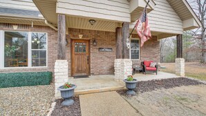 A brick house with a porch, a flag, and a red chair. - < 5 Mi to Lake Desoto: Grand Hot Springs Home (Hot Springs Village)