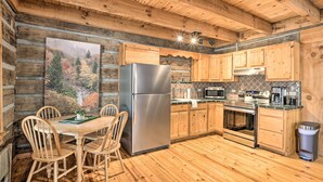 L’intérieur d’un chalet en bois comprend un coin repas, une cuisine et un grand tableau représentant une scène de forêt.