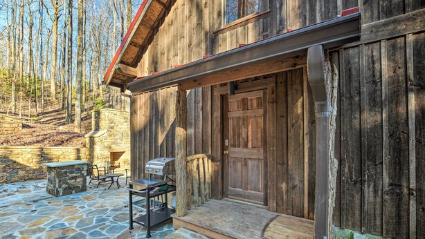Une cabane en bois rustique avec un patio en pierre, une porte en bois et un petit espace extérieur aménagé pour s’asseoir.