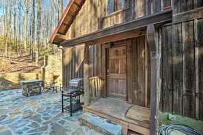 Une cabane en bois rustique avec un patio en pierre, une porte en bois et un petit espace extérieur aménagé pour s’asseoir.