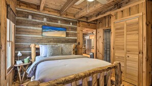 Une chambre dans un chalet en rondins, avec un lit, des murs en bois, un ventilateur de plafond et un tableau accroché au mur.
