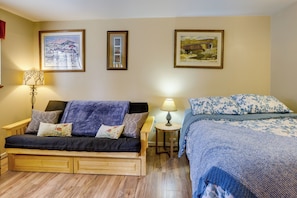 A cozy room with a wooden sofa, a bed with a blue floral bedspread, and two framed pictures on the wall. - Sunriver Vacation Rental w/ Community Hot Tub! (Bend)