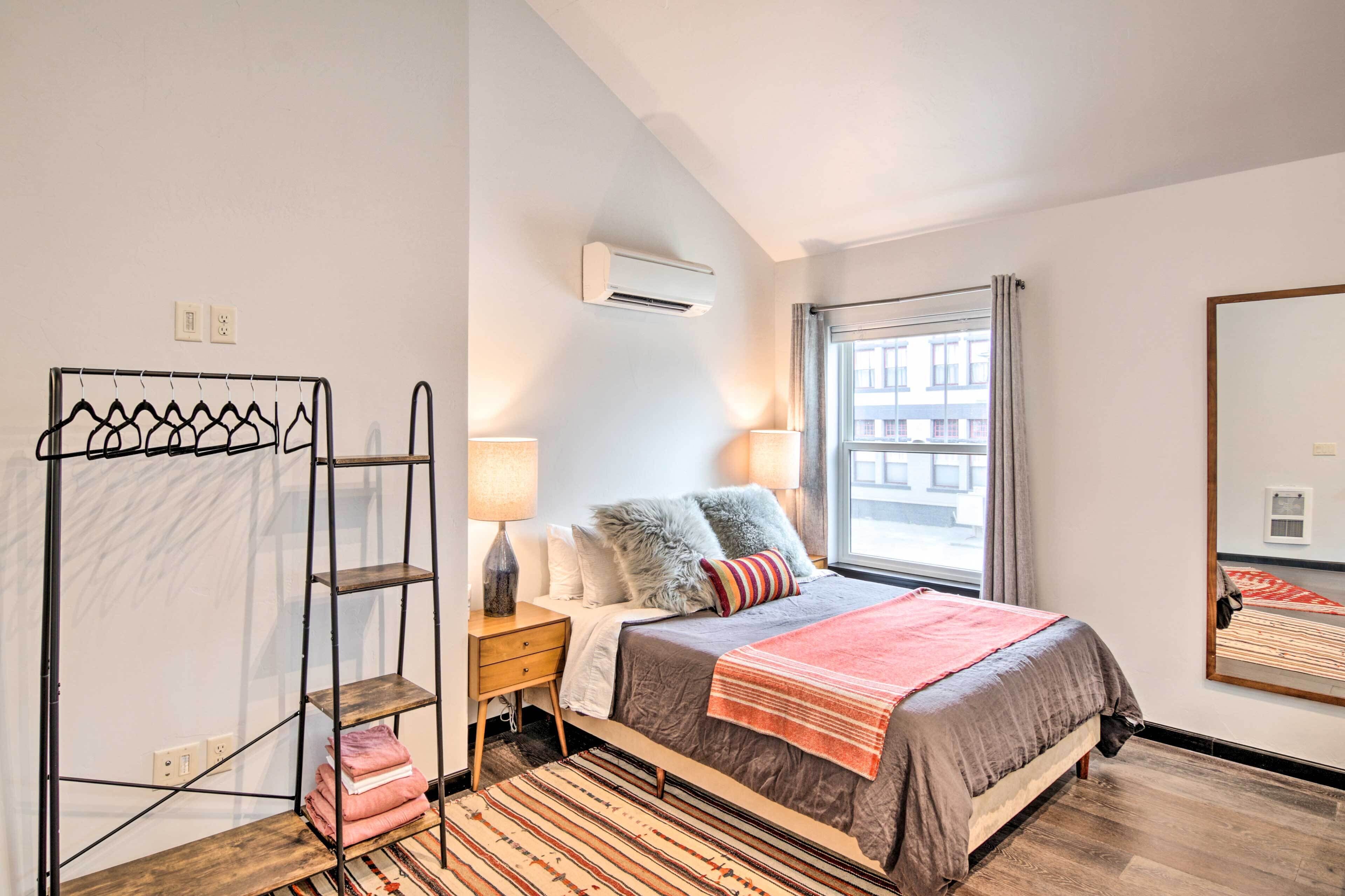 A bedroom with a bed, nightstands, a metal rack, a window with curtains, and an air conditioning unit.