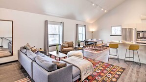 A modern living room with a grey sofa, a dining area with a table and chairs, and a kitchen with a refrigerator and stove. - Contemporary-boho Loft in Downtown Livingston! (Livingston)